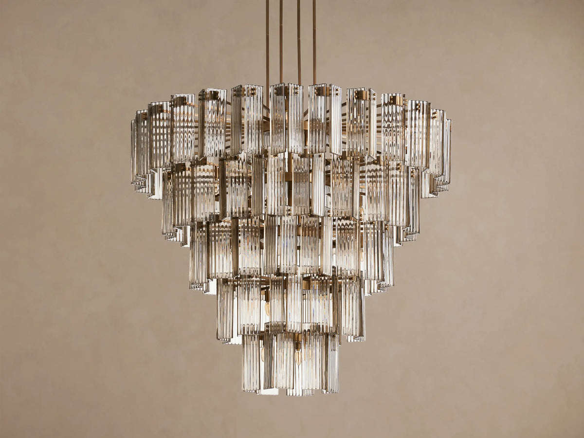 Delsie Round Chandelier: tiered clear glass rods catch light, warm glow from within, burnished brass finish, neutral wall.