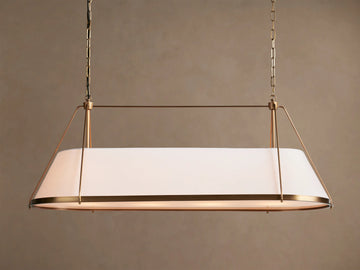 Shelton Linear Chandelier with burnished brass frame & illuminated tapered white linen shade, hanging from chains.