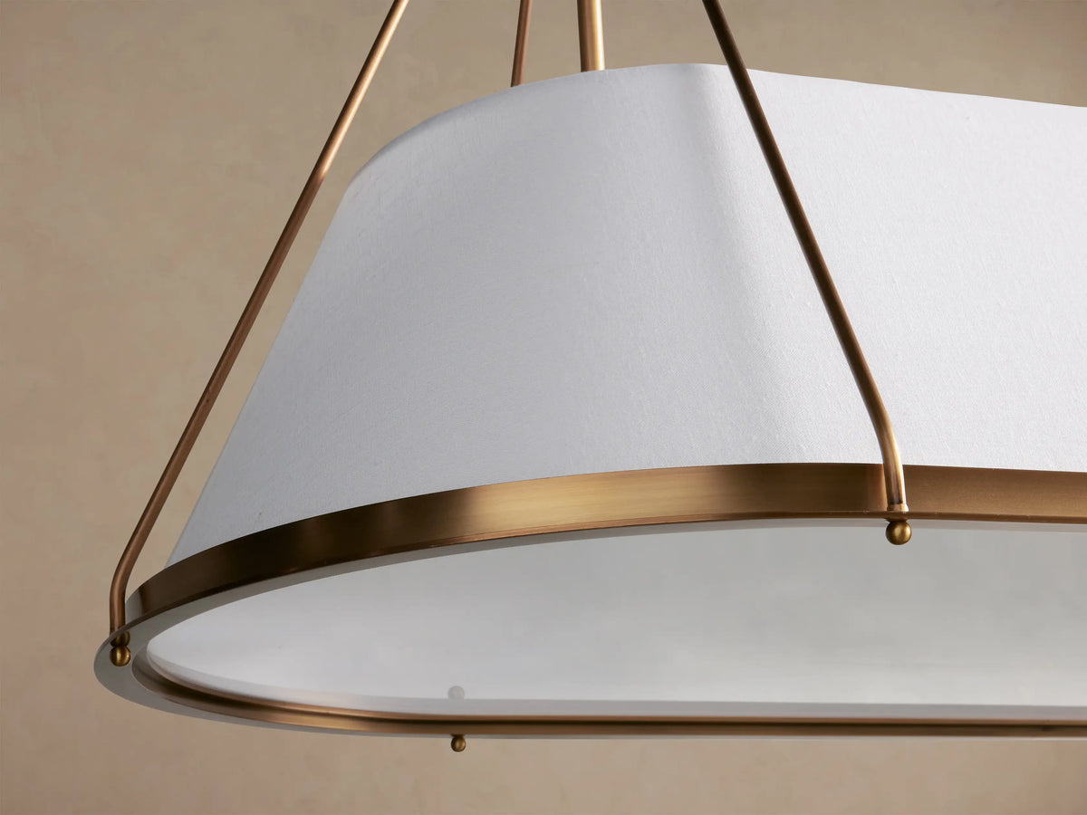 Shelton Linear Chandelier with burnished brass frame, rectangular white tapered linen shade, hanging from two brass chains.