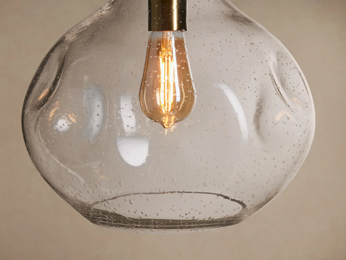 Close-up of Organic 12" Pendant with an irregularly shaped, clear seeded glass shade & illuminated filament bulb.