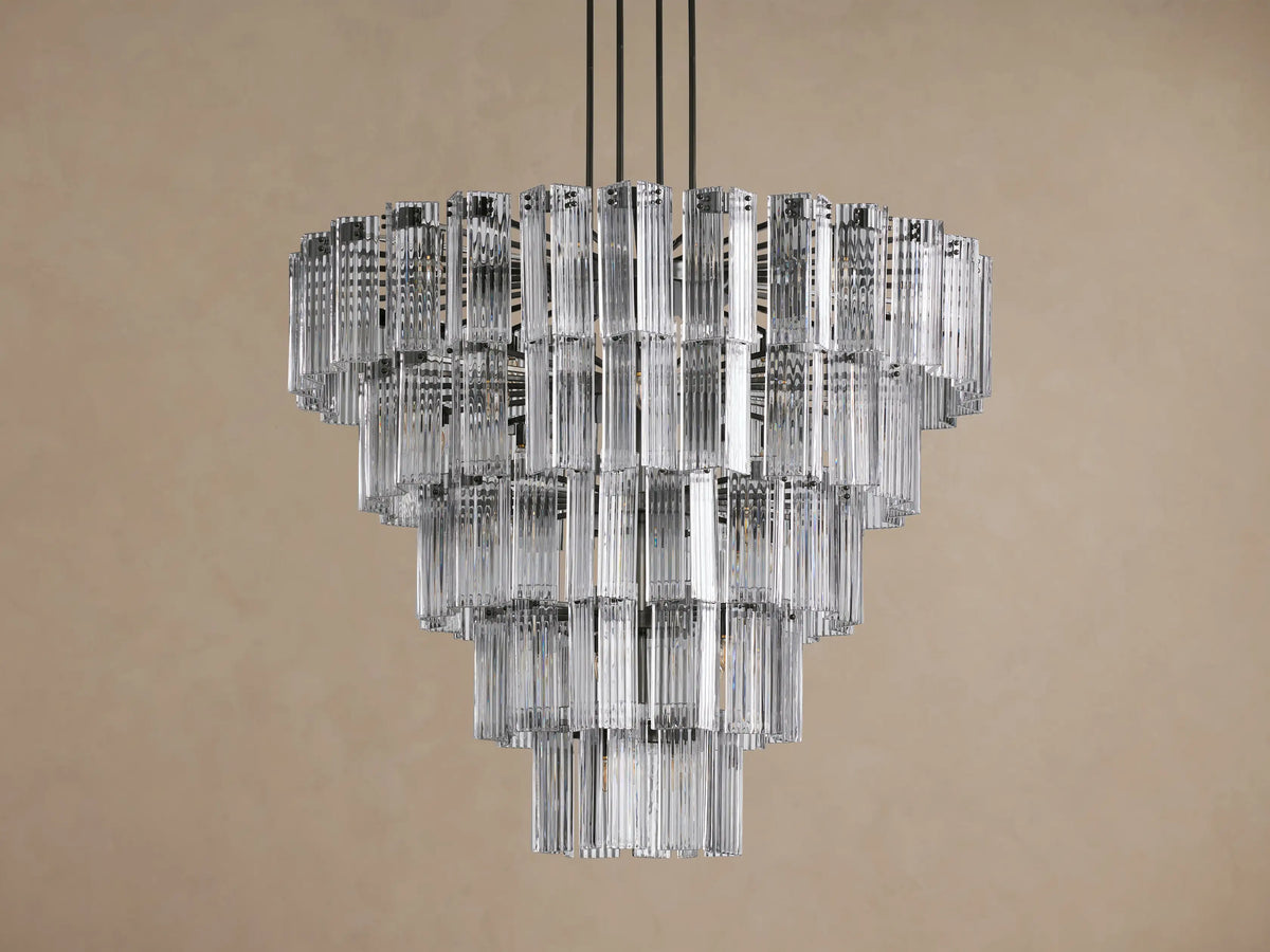 Delsie Round Chandelier, multi-tiered with clear fluted glass rods and dark frame, glowing brightly against a plain background.