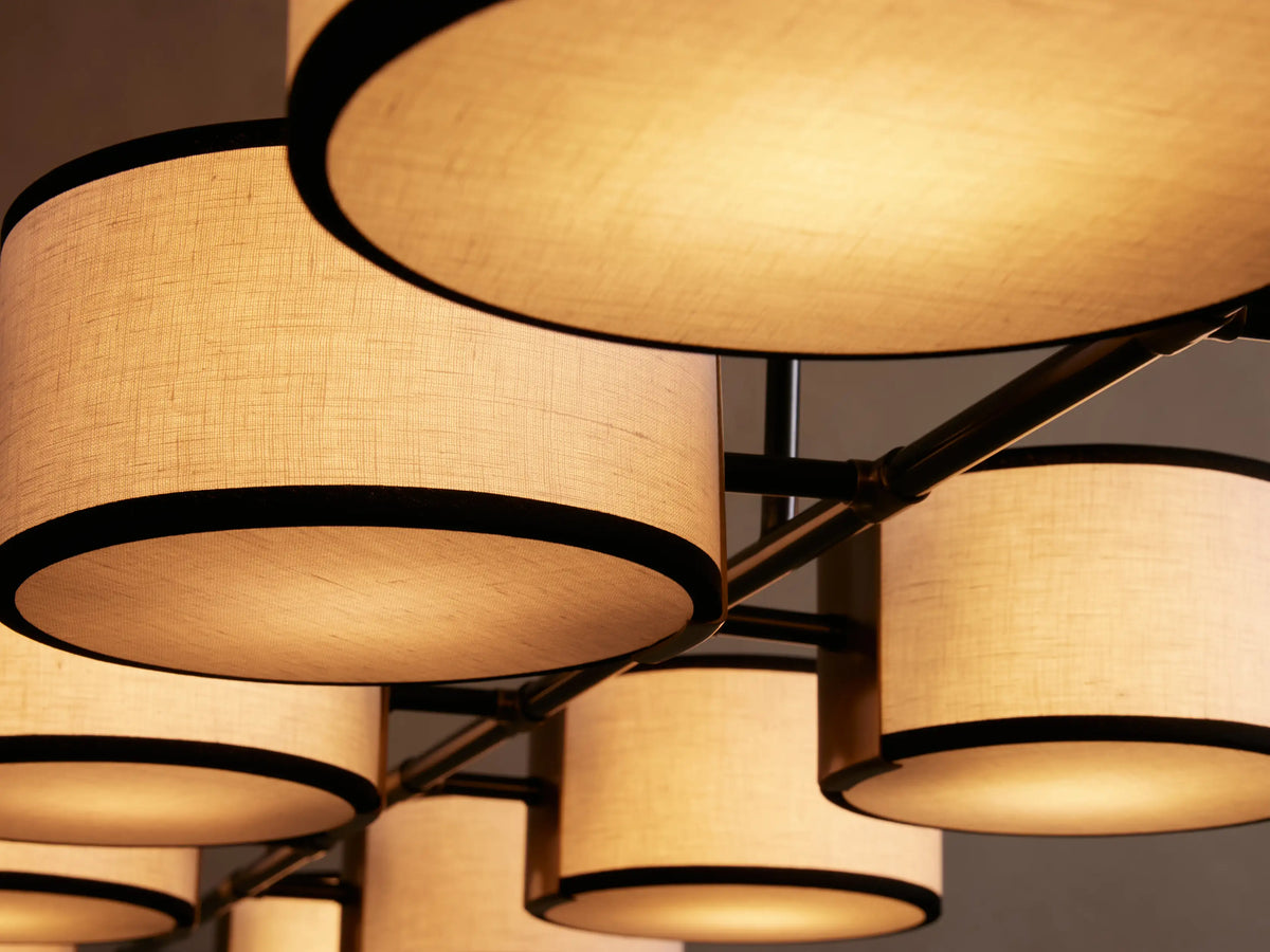 Eight cylindrical pendant lights with white shades and black trim, suspended in a row from a ceiling, on a beige background.