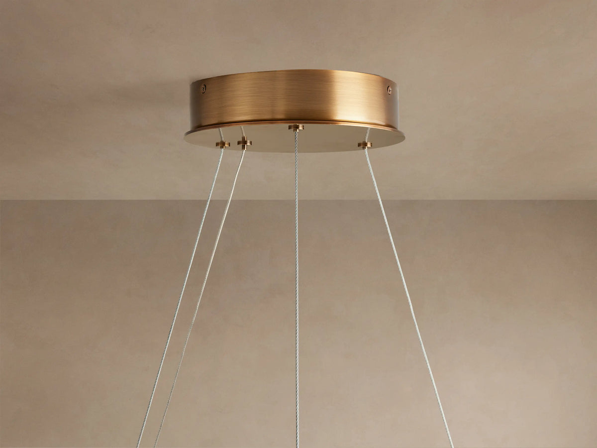 Halo-shaped chandelier with a warm glow, crafted from Spanish alabaster stone. Features brass accents and steel cables for mounting.
