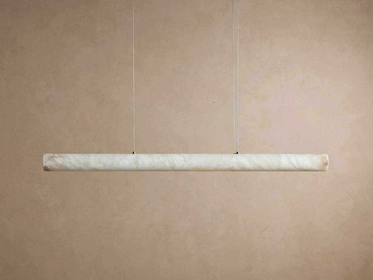 Halima Linear Chandelier with glowing alabaster stone, elongated horizontal bar, suspended by thin steel cables against a beige background.