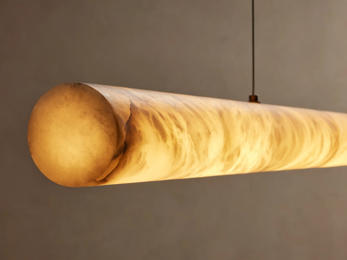 Halima Linear Chandelier with alabaster stone cylinder suspended by two steel cables against a plain beige background.