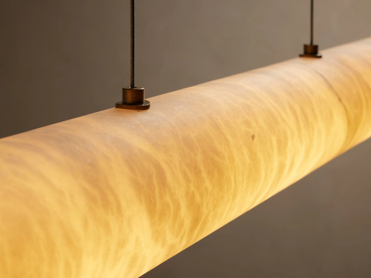Halima Linear Chandelier made of Spanish alabaster stone with warm amber glow, suspended by steel cables against a neutral background.