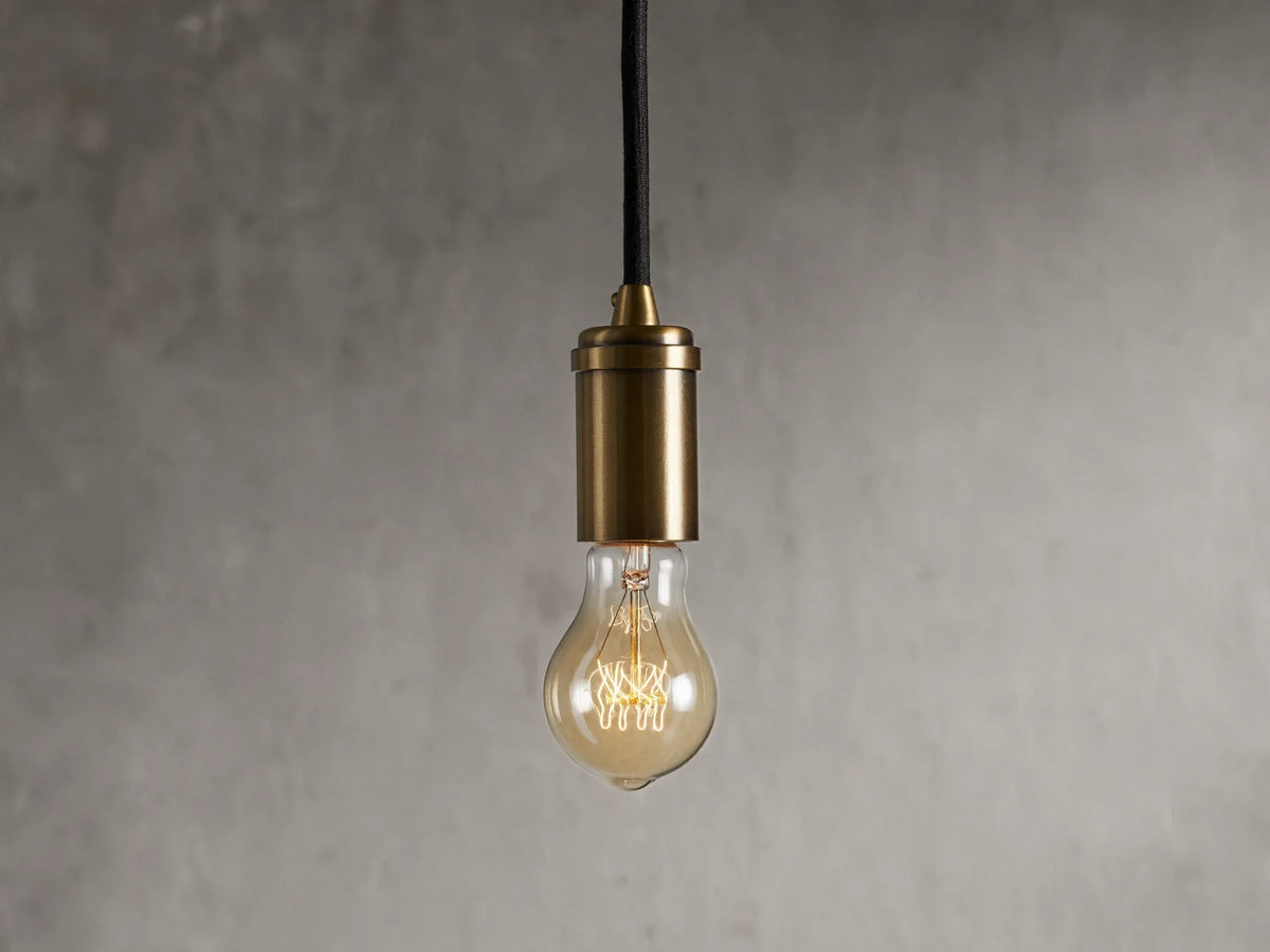 Ohlson Brass Swag Pendant with a brass-plated finish, hanging against a textured gray background.