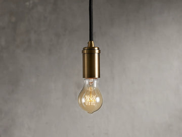 Ohlson Brass Swag Pendant with a brass-plated finish, hanging against a textured gray background.