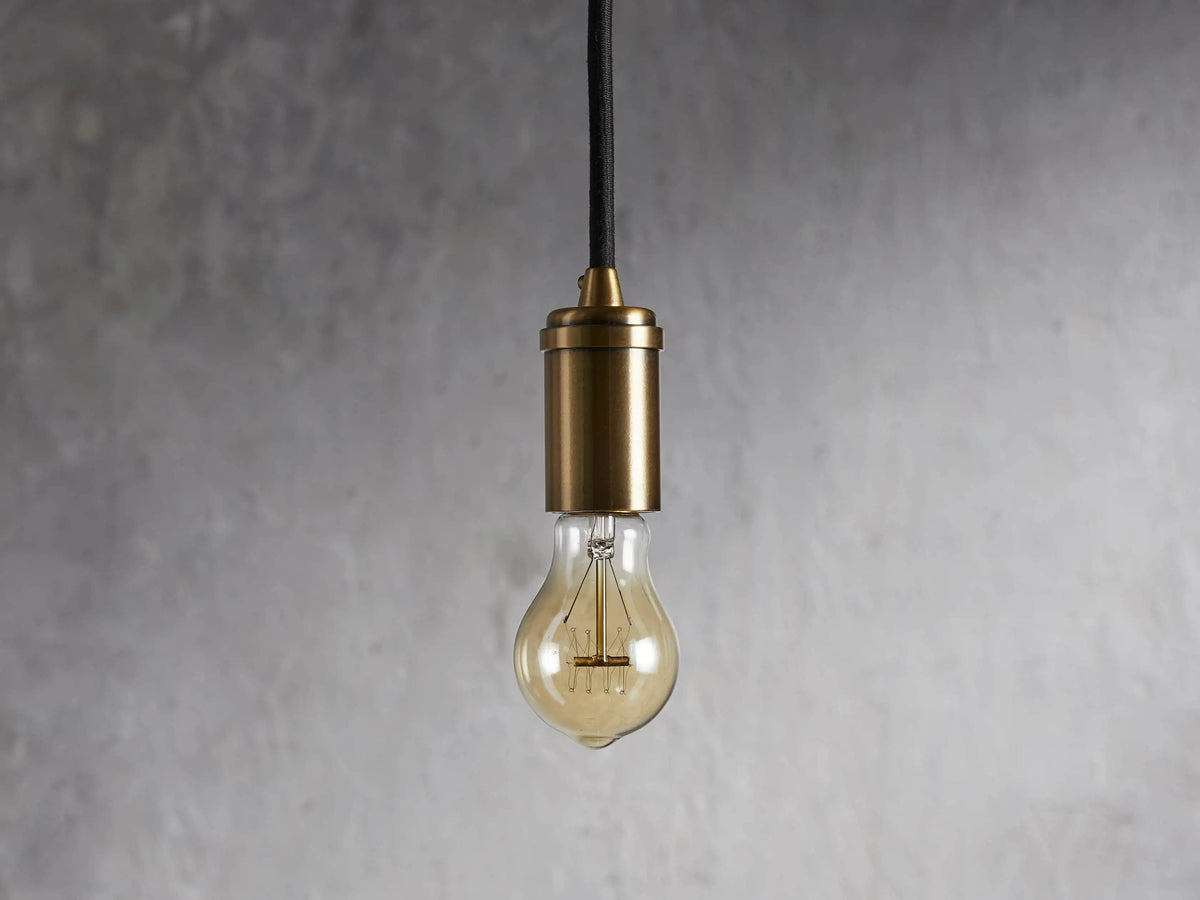 Ohlson Brass Swag Pendant with a brass-plated finish, hanging against a textured gray background.