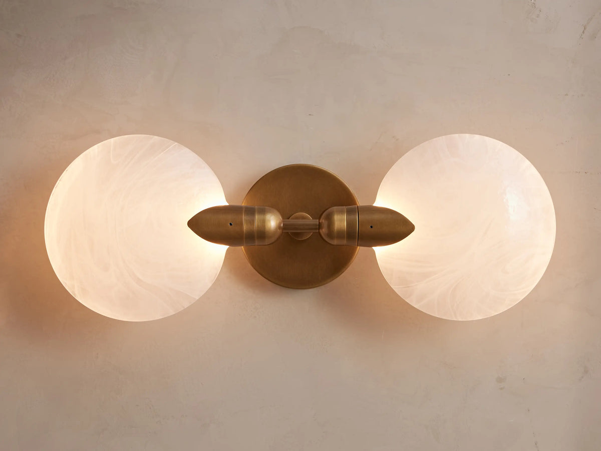 Lyla Double Sconce with hand-blown glass globes and brass plate, mounted vertically on a wall, with a soft glow.