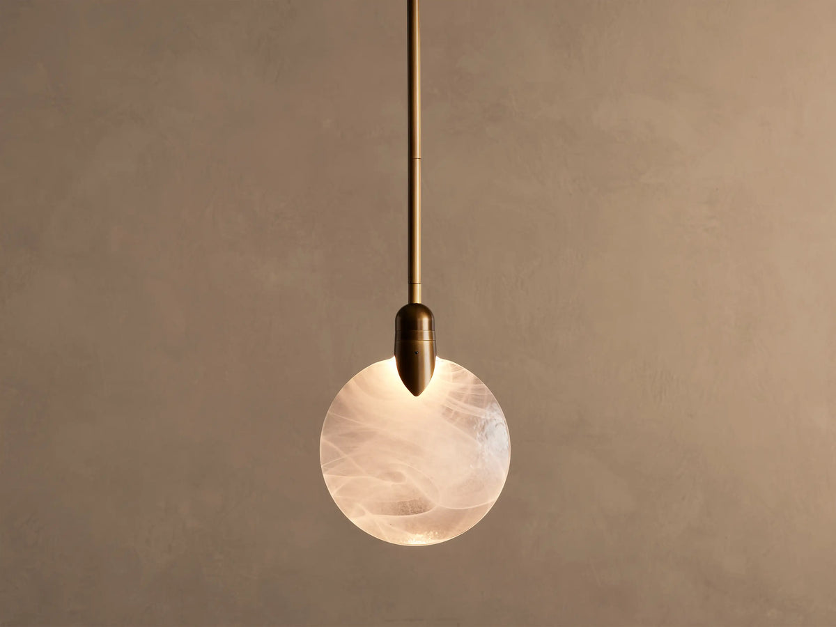 Lyla Single Pendant, a brass-plated fixture with a glowing, spherical hand-blown glass shade featuring white swirls.