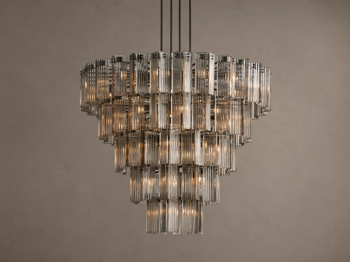 Delsie Round Chandelier, tiered with many illuminated clear fluted glass rods, suspended against a warm brown wall.