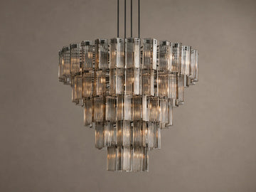 Delsie Round Chandelier, tiered with many illuminated clear fluted glass rods, suspended against a warm brown wall.