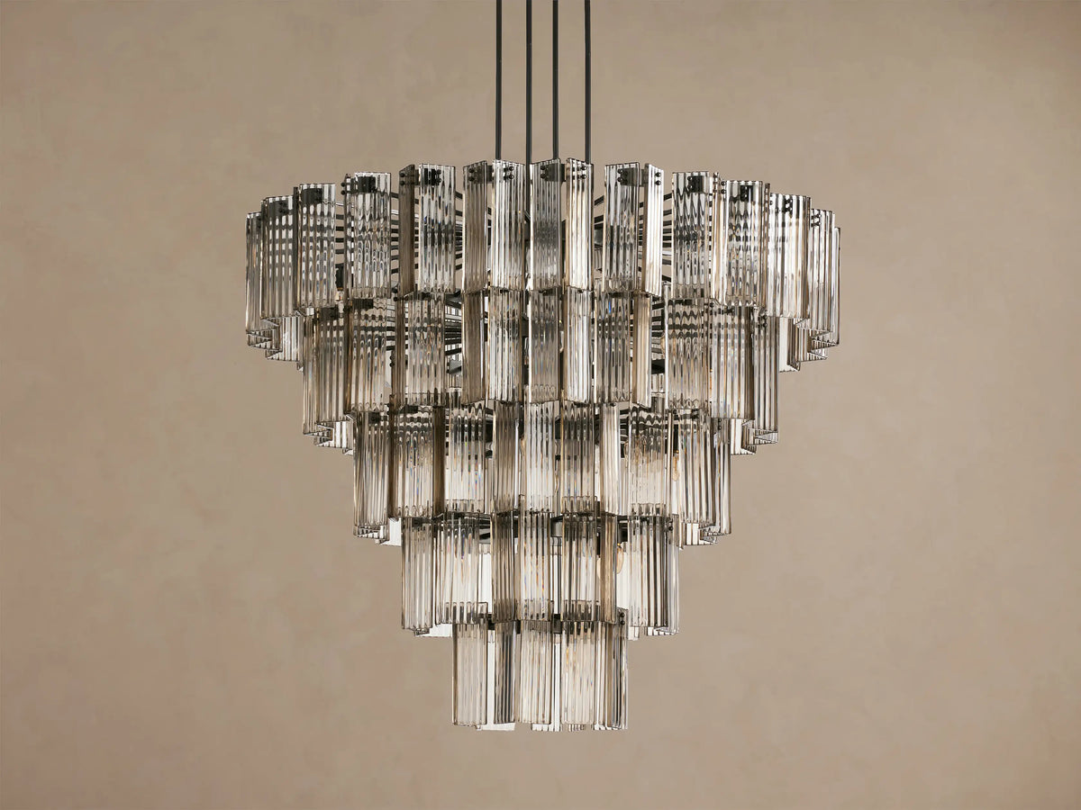 Delsie Round Chandelier, tiered with many illuminated clear fluted glass rods, suspended against a warm brown wall.