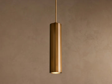 A cylindrical pendant light with a glossy brass finish hangs from the ceiling against a plain beige background.