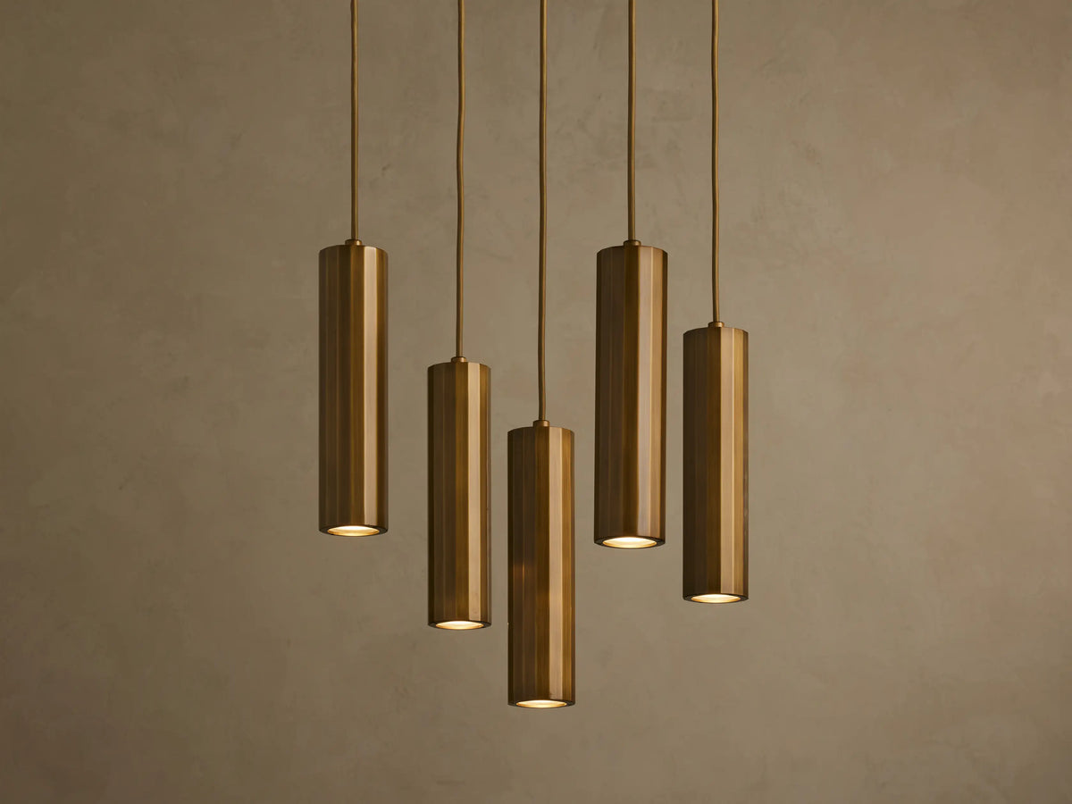 Five bronze cylindrical pendant lights hanging in a staggered arrangement against a textured beige wall.