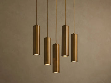 Five bronze cylindrical pendant lights hanging in a staggered arrangement against a textured beige wall.