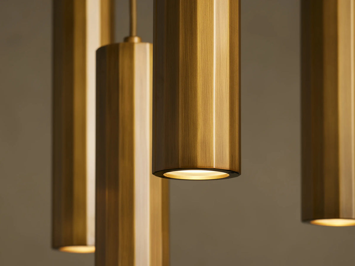 Four cylindrical bronze pendant lights with a brushed texture, hanging from the ceiling against a neutral background. The lights are illuminated.