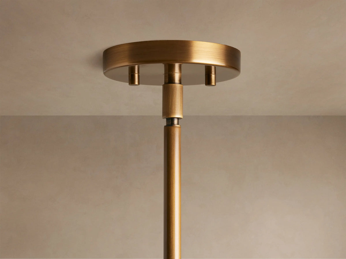 Bronze pendant light fixture with a frosted glass shade, featuring a spherical design, casting a warm glow against a soft brown background.
