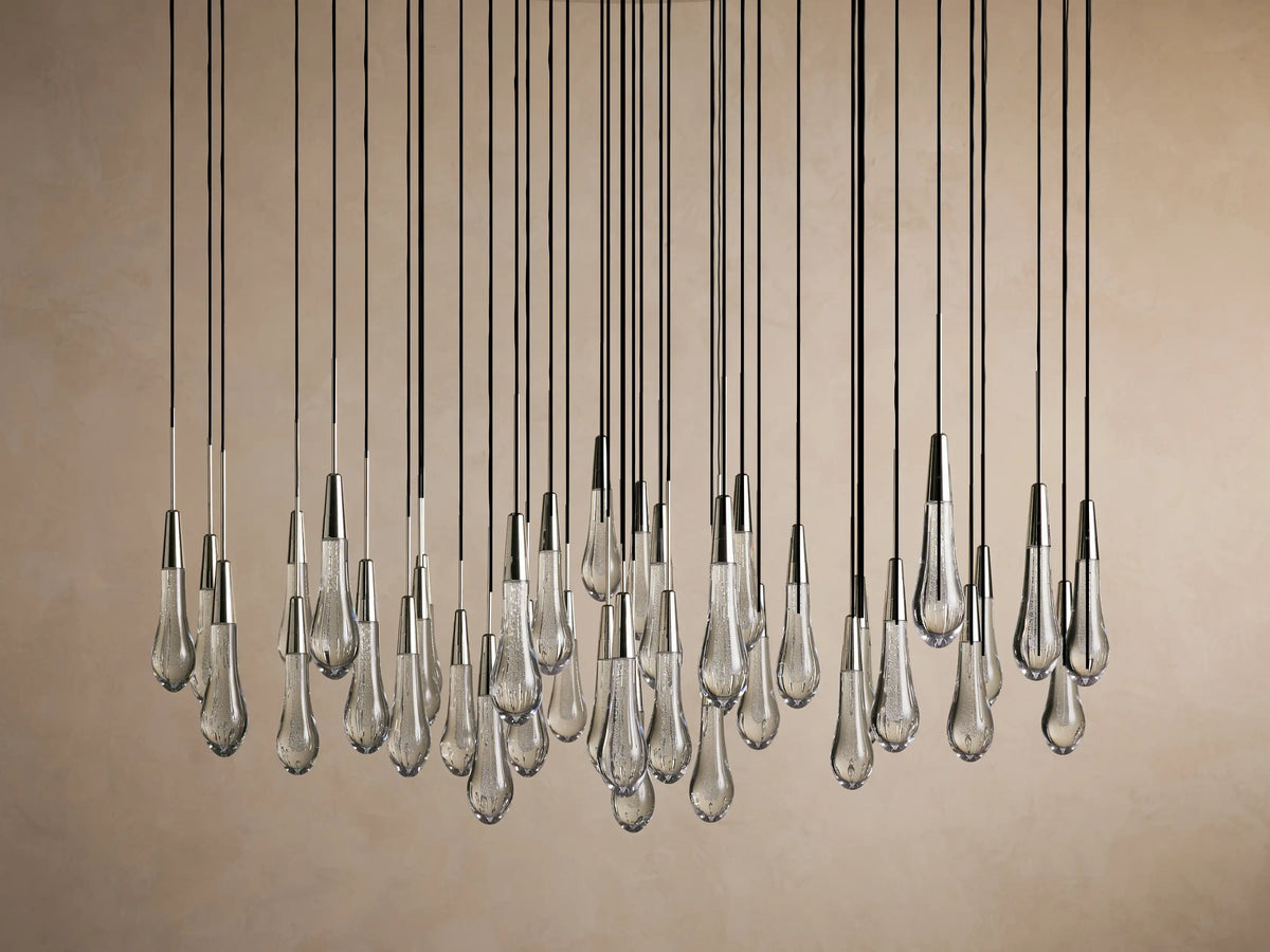 A cluster of teardrop-shaped LED bulbs hangs from black cords, creating a sparkling Soltaire Round Chandelier against a soft brown background.