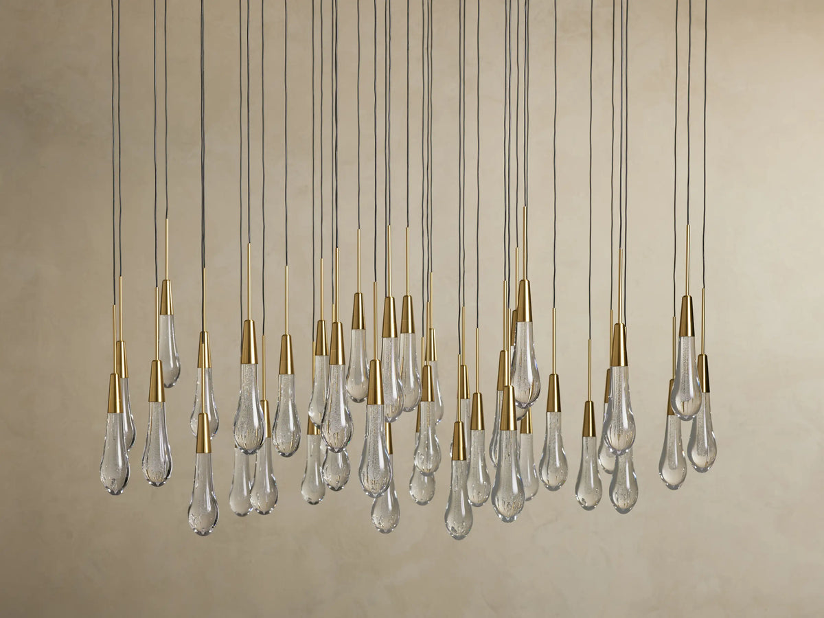 Clear teardrop-shaped glass pendants with brass caps hang in varying lengths from thin cords on the Soltaire Round Chandelier.
