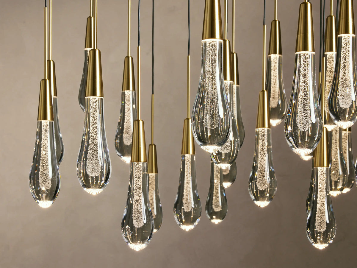 Soltaire Round Chandelier with multiple elongated teardrop-shaped glass pendants, featuring brass-finished tops and visible LED bulbs inside.