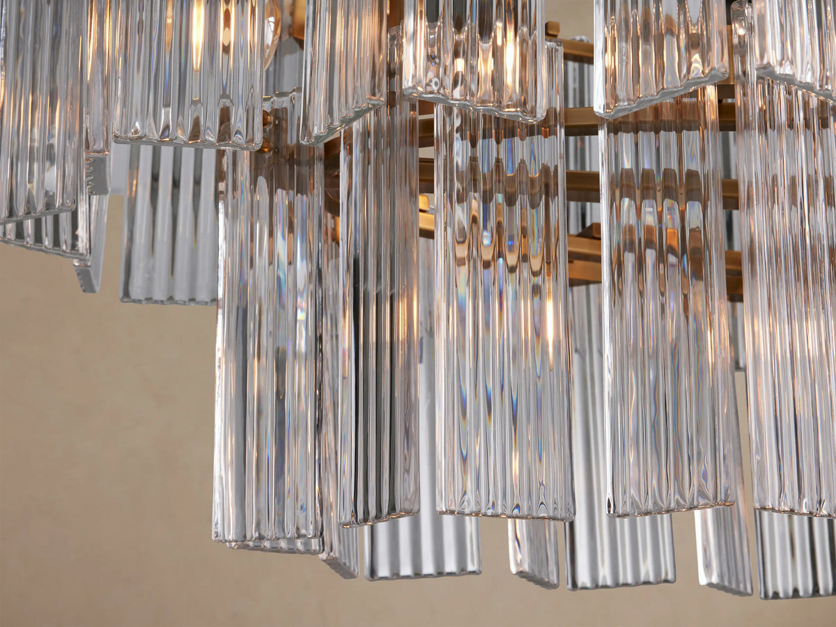 Delsie Oval Tiered Chandelier featuring clear ribbed glass panels, burnished brass frame, suspended on a plain background.