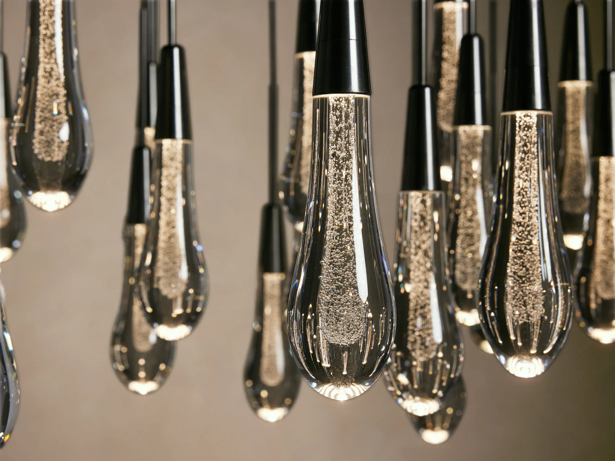 Close-up of the Soltaire Round Chandelier, featuring elongated teardrop-shaped bulbs with black tops and clear glass, suspended from black cords.