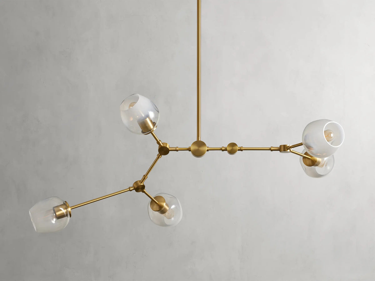 Brass chandelier with five arms, matte finish, globe-shaped glass shades, minimalist design, suspended from a central rod.