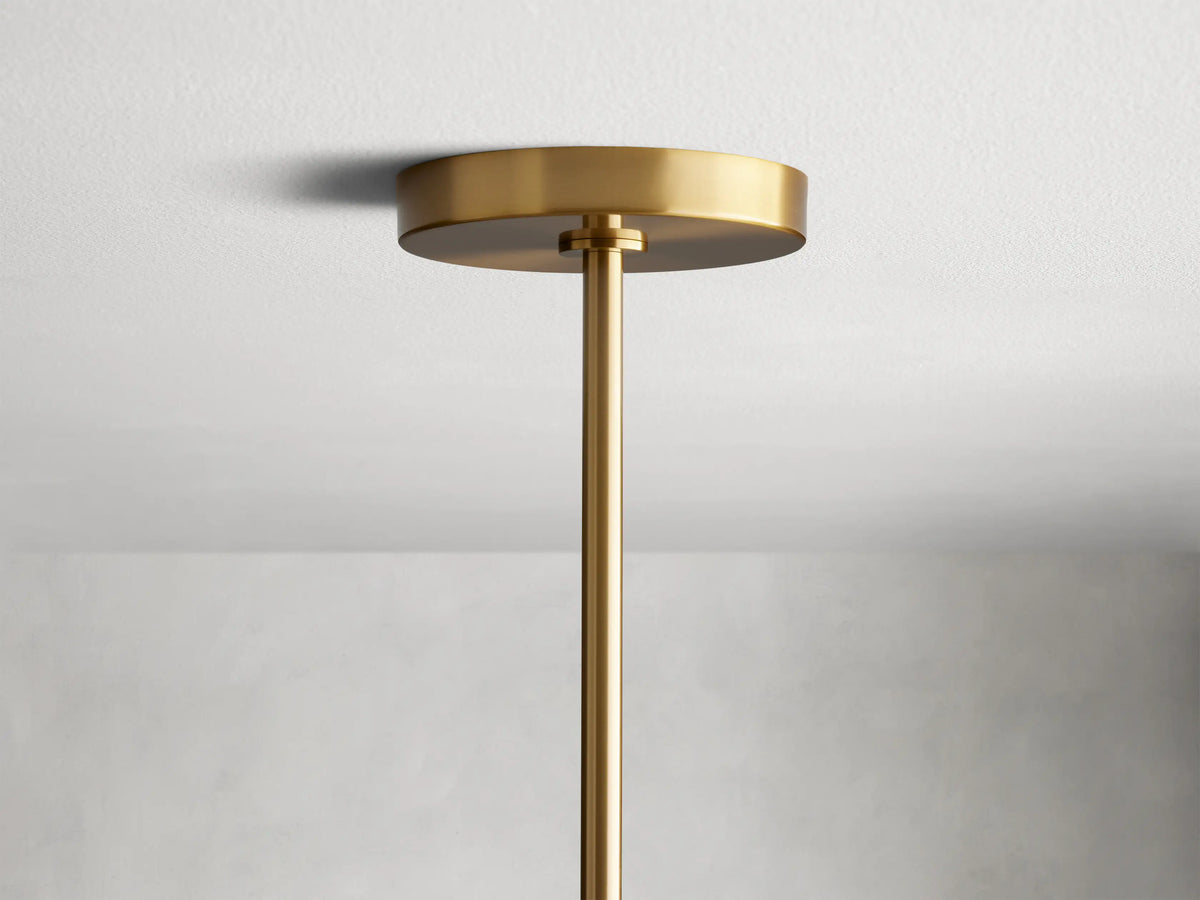Noella Brass Chandelier with a glass globe encasing a partially illuminated bulb, mounted on a matte brass arm against a light background.