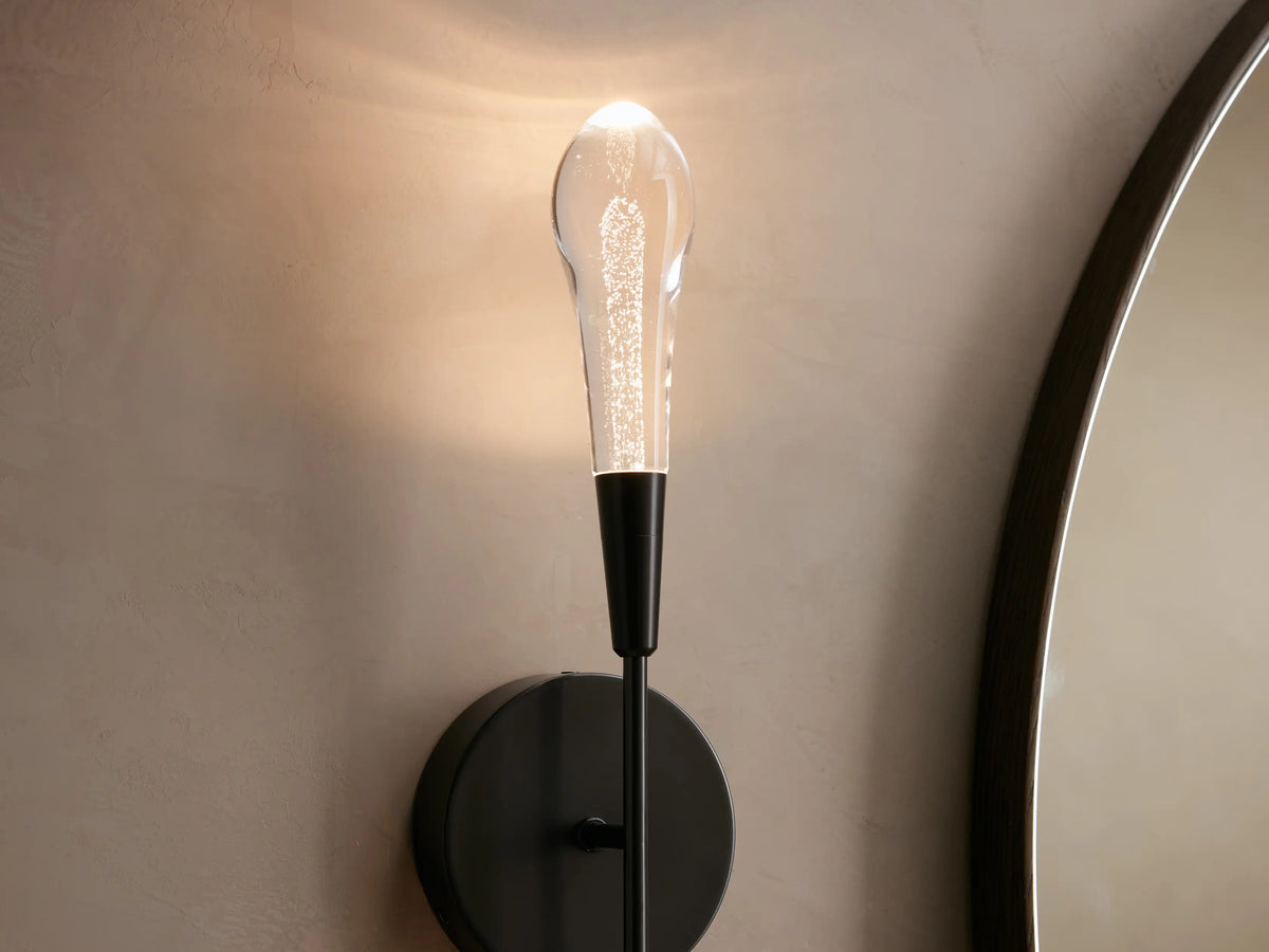 Double sconce with black round backplate, vertically aligned clear glass rods extending above and below on a beige wall.