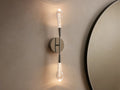 Soltaire Double Sconce mounted on a wall, features two teardrop LED bulbs on a polished nickel backplate, emitting warm light.