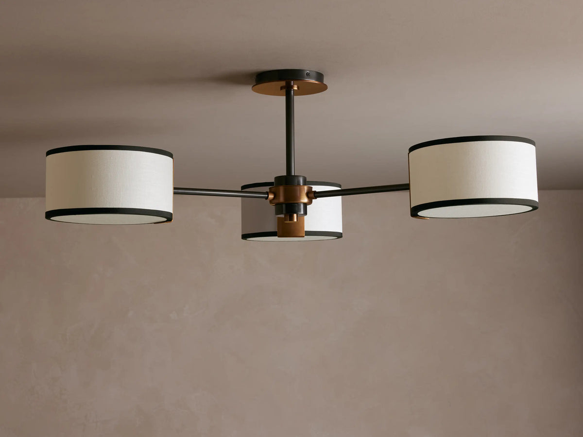 Daphne Flush Mount: 3 white linen shades with black trim, dark bronze frame, lit against a grey ceiling.