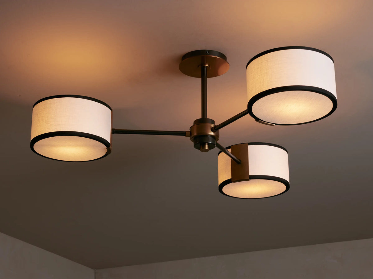 Close-up of Daphne Fabric Flush Mount. Bronze central fixture, dark arms, two illuminated white linen shades with black trim.