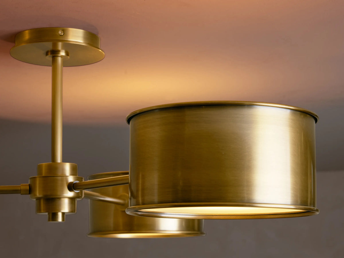 Daphne Metal Flush Mount in antique brass. Three cylindrical shades extend from a central rod, flush mounted on a ceiling.
