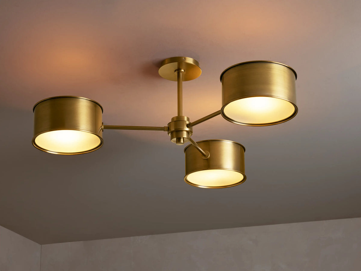 Daphne Metal Flush Mount, antique brass finish, with multiple arms & cylindrical shades emitting warm light from a ceiling.