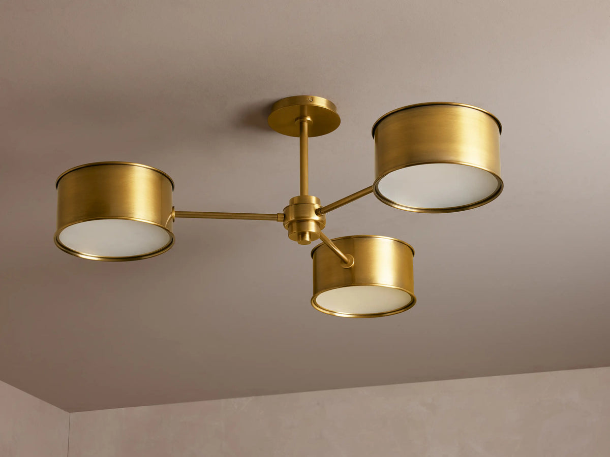 Daphne Metal Flush Mount: 3-light antique brass ceiling fixture with cylindrical shades, casting a warm glow.