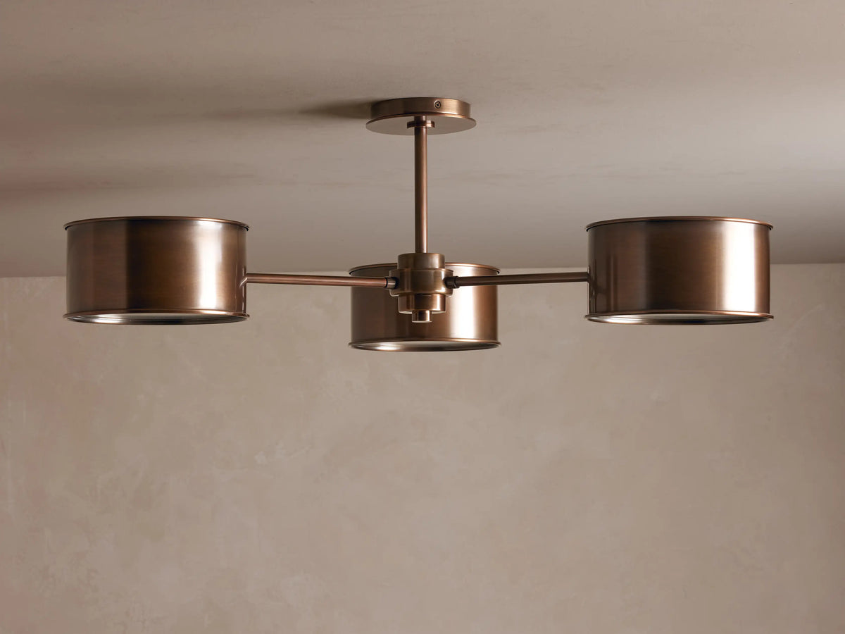 Daphne Metal Flush Mount in warm bronze with three cylindrical shades casting a soft, warm glow on a light ceiling.