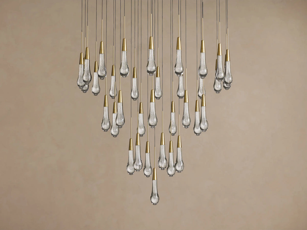 Soltaire Round Chandelier: cascading clear glass bubble pendants with shiny brass caps against a light beige wall.