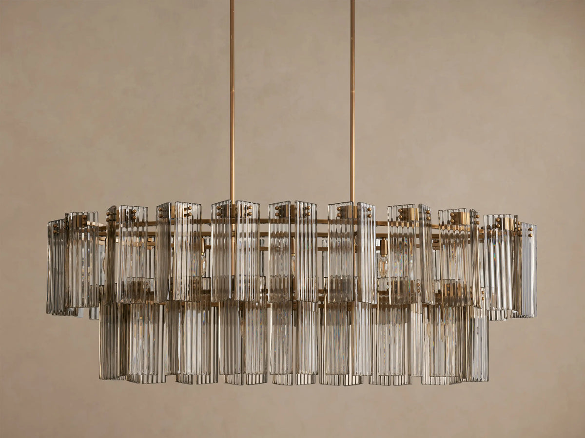 Delsie Oval Tiered Chandelier: illuminated bulbs shine through two tiers of clear, ribbed glass panels on a brass frame.