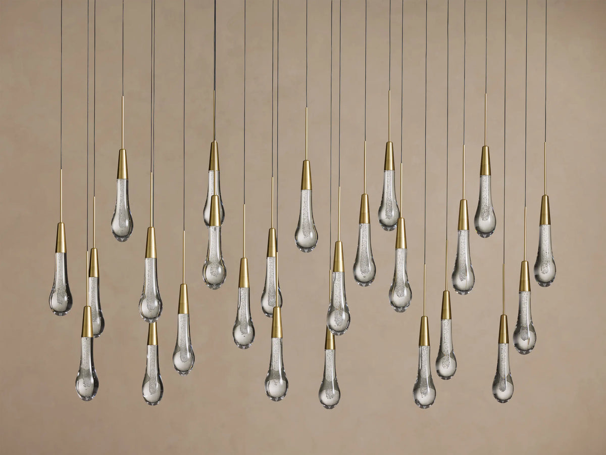 Soltaire Linear Chandelier: Many clear, teardrop-shaped glass pendants with internal bubbles & brass caps, hanging.