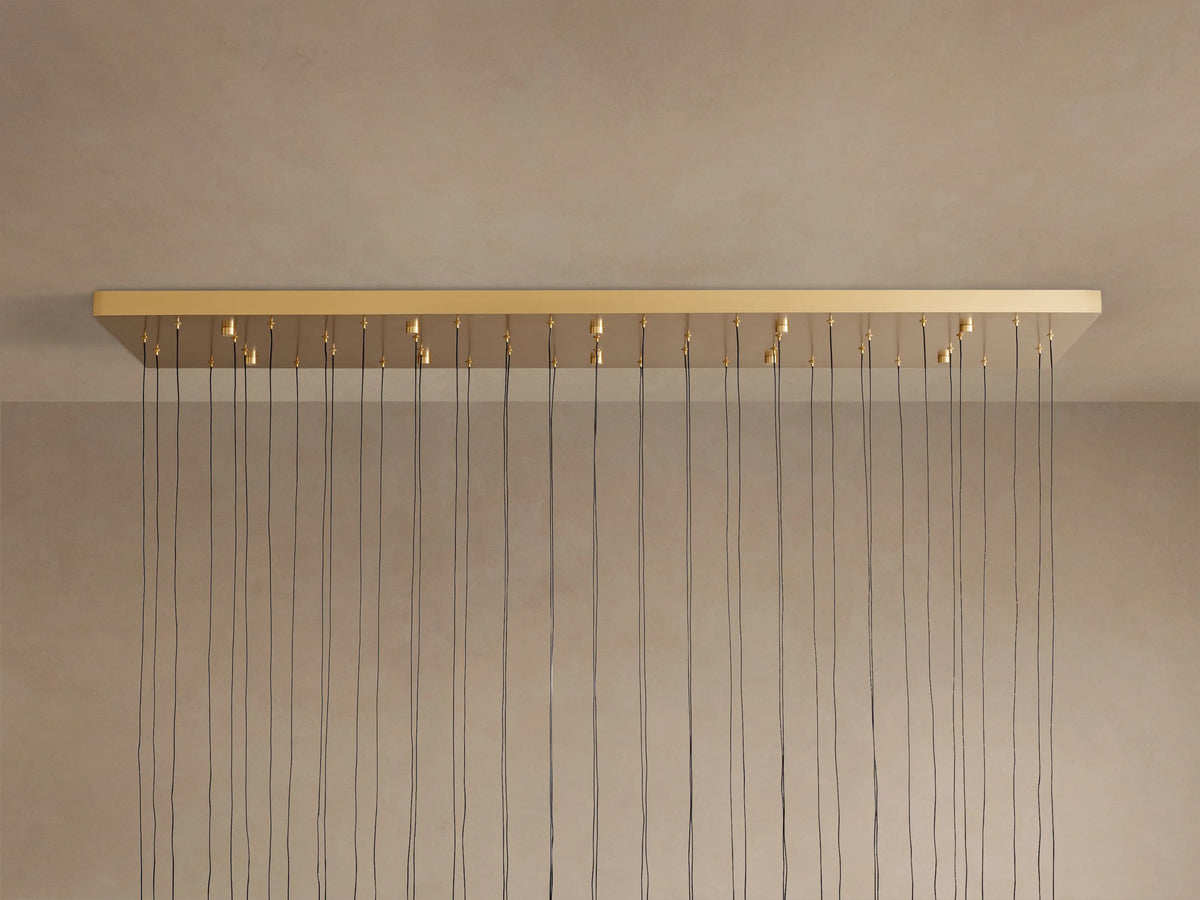 Brass-finished Soltaire Linear Chandelier base mounted on a beige ceiling, with numerous black suspension cords hanging vertically.
