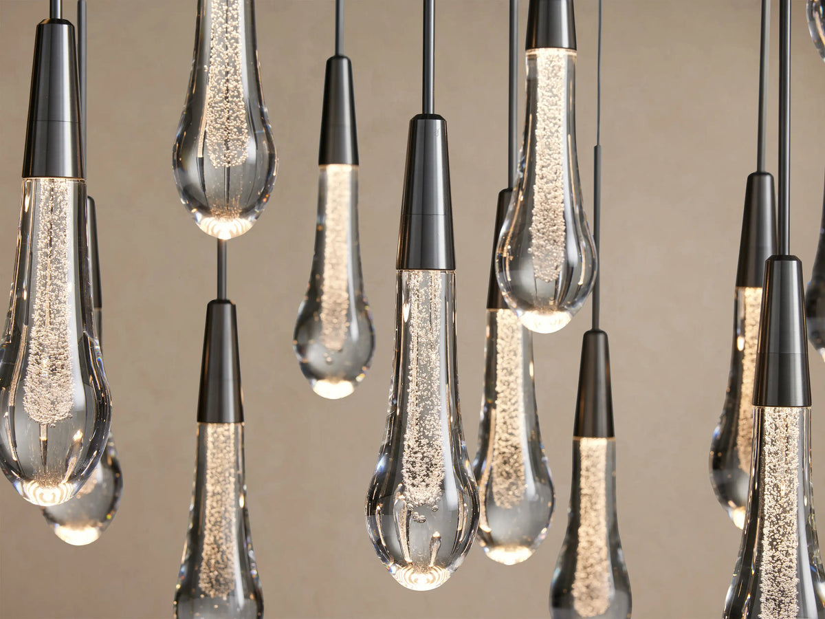 Close-up of Soltaire Round Chandelier with multiple teardrop clear glass pendants, dark metal tops, glowing LED bubbles inside.