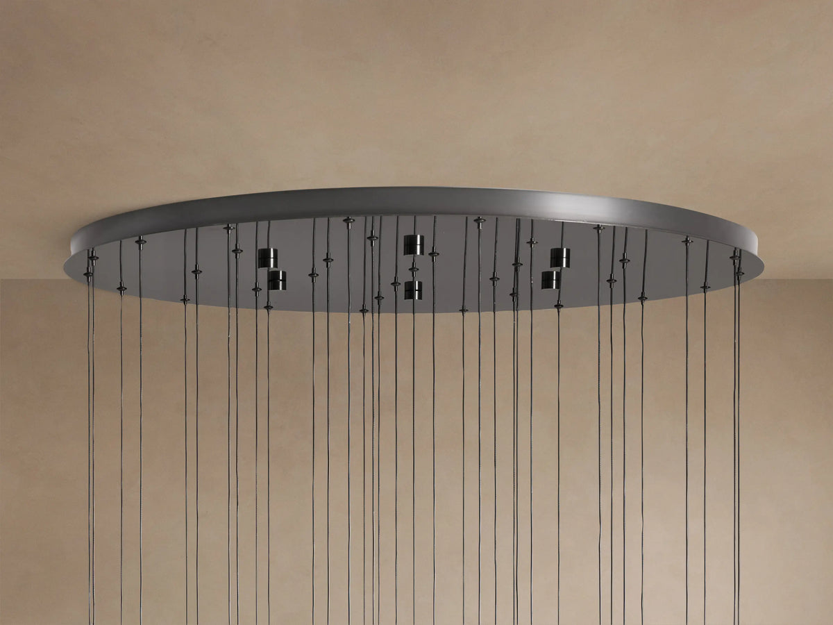Underside of a dark gray/bronze Soltaire Round Chandelier canopy with many thin black cords hanging down against a light wall.