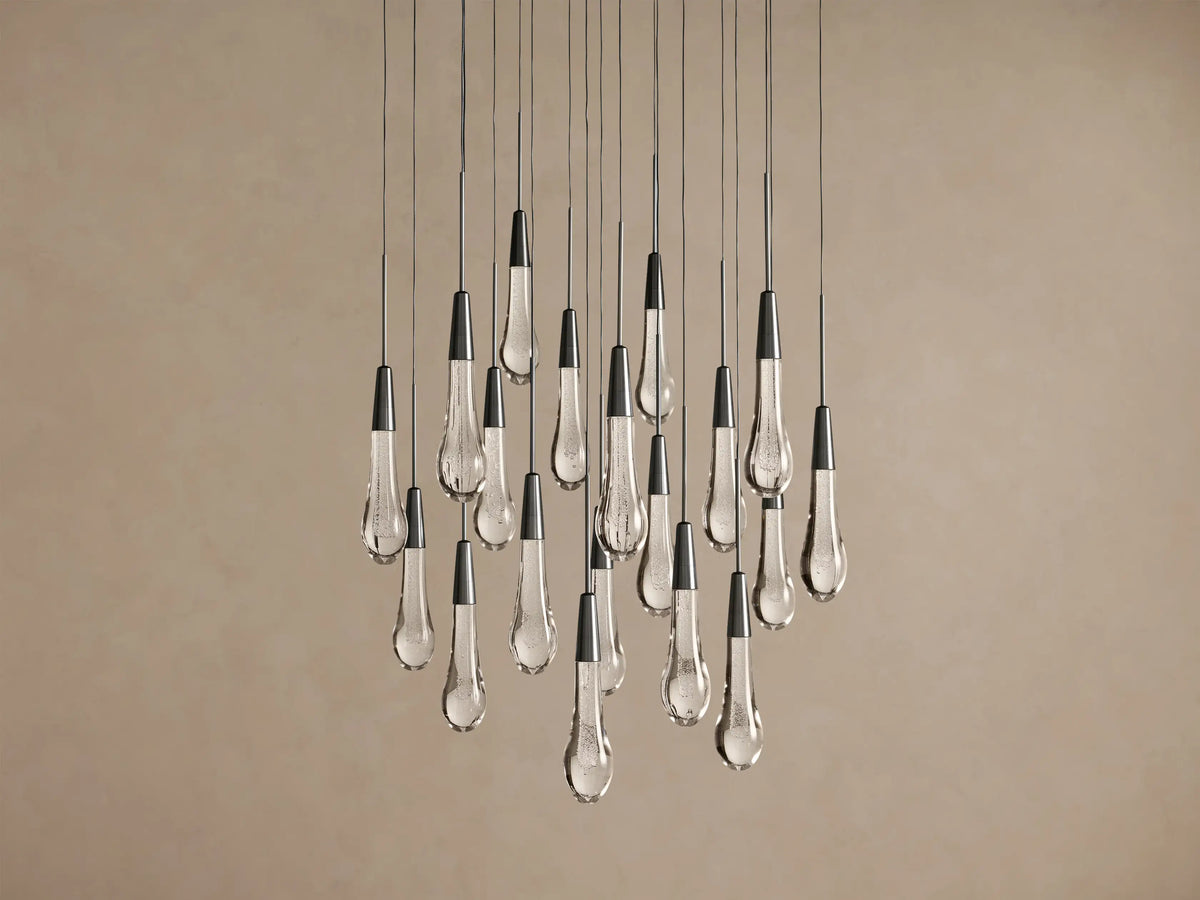 Soltaire Round Chandelier with multiple clear glass teardrop pendants, dark conical tops, hanging against a light brown wall.