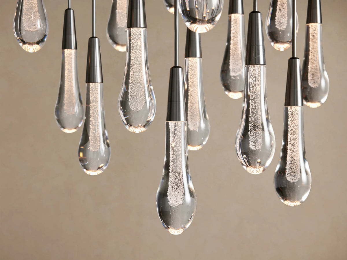 Soltaire Round Chandelier: Clear, bubbly teardrop pendants with dark metallic caps, illuminated against a light background.