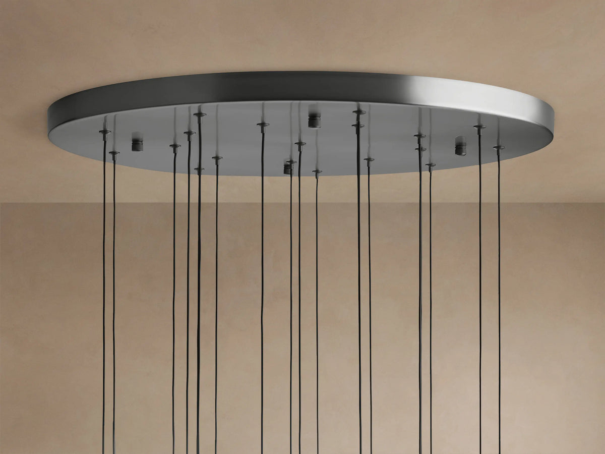 Soltaire Round Chandelier ceiling plate in brushed metal finish with many thin black cords hanging down against a beige ceiling.