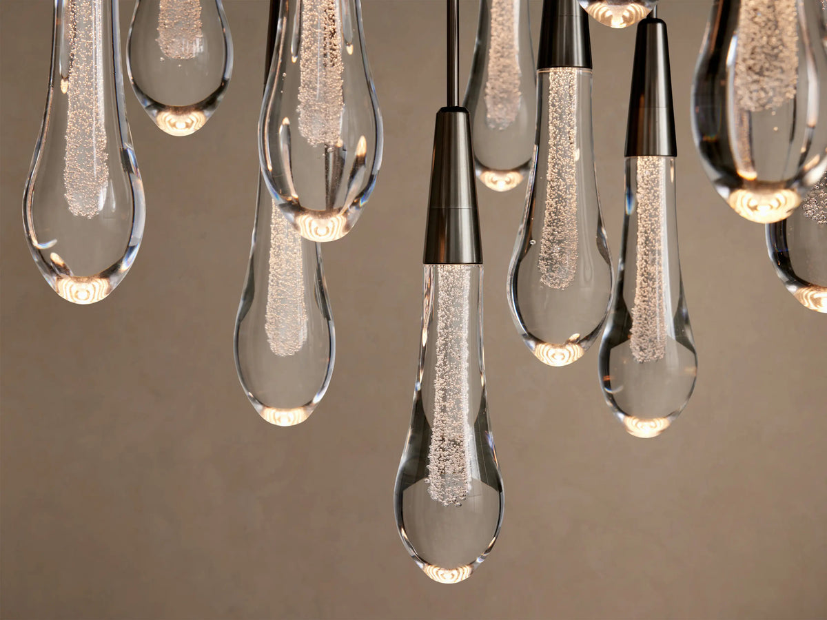 Soltaire Round Chandelier close-up: clear glass teardrop pendants with bubbly illuminated centers, dark metal caps.