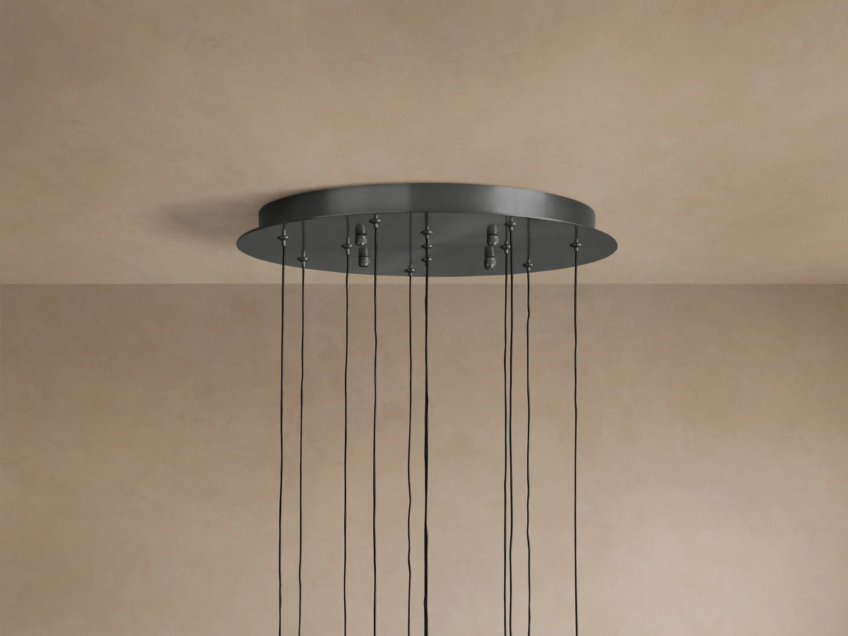 Soltaire Round Chandelier's dark metallic round ceiling canopy with multiple black cords hanging down, against a beige ceiling.
