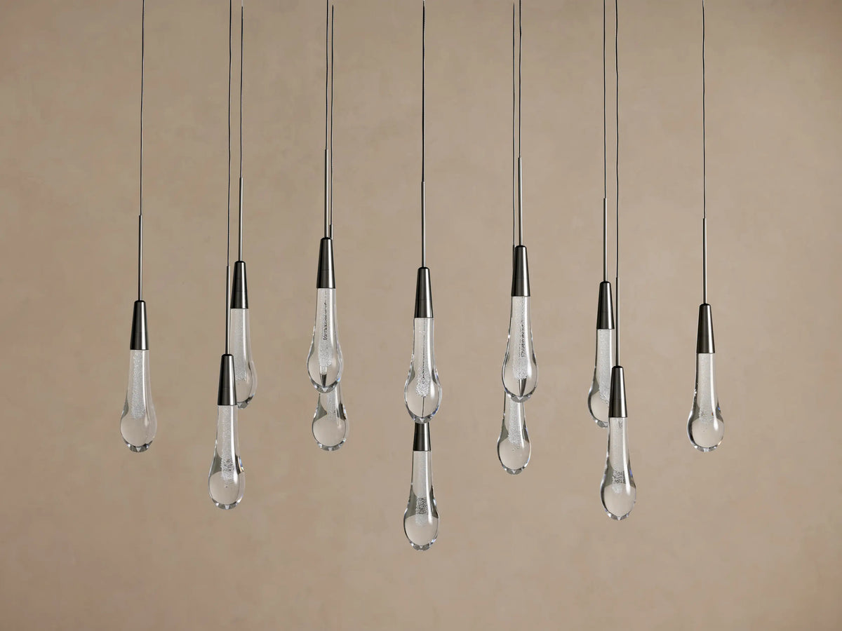 Soltaire Linear Chandelier with multiple clear glass teardrop pendants suspended at various heights from dark metal fixtures.